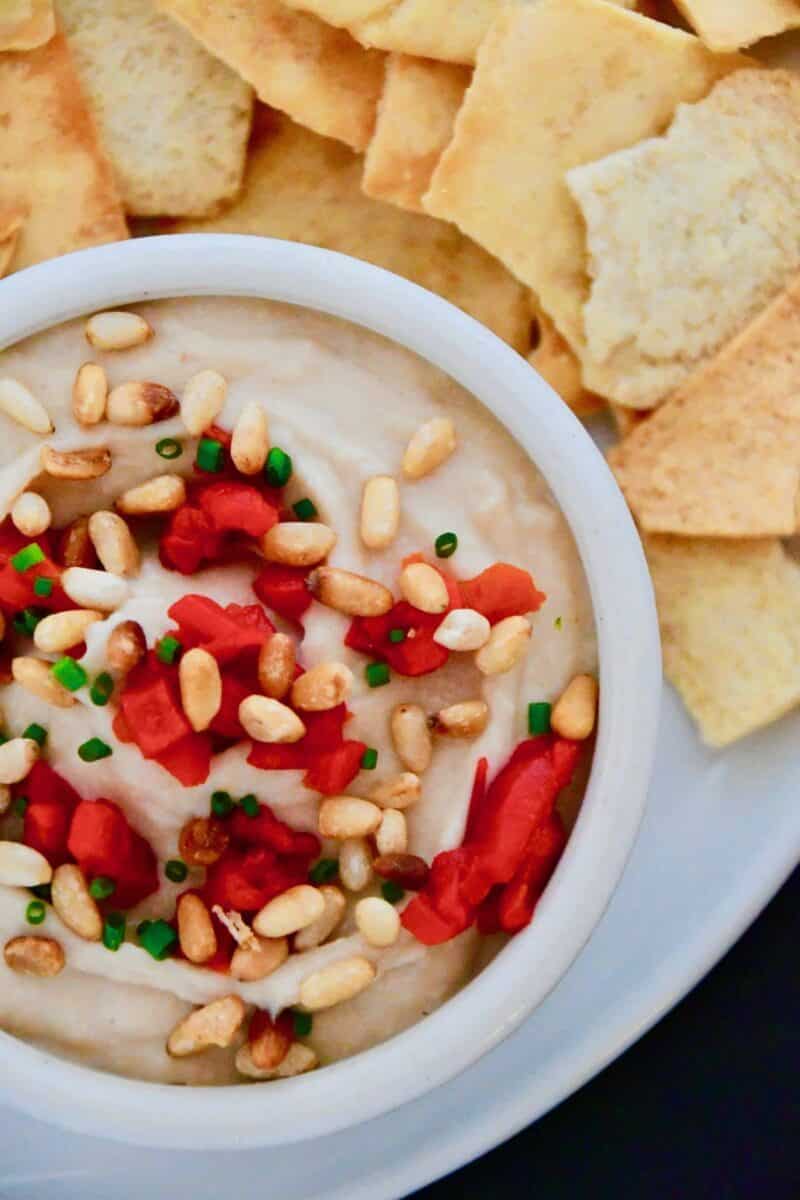Joanna Gaines White Bean Hummus in a bowl topped with extra pine nuts and red peppers.