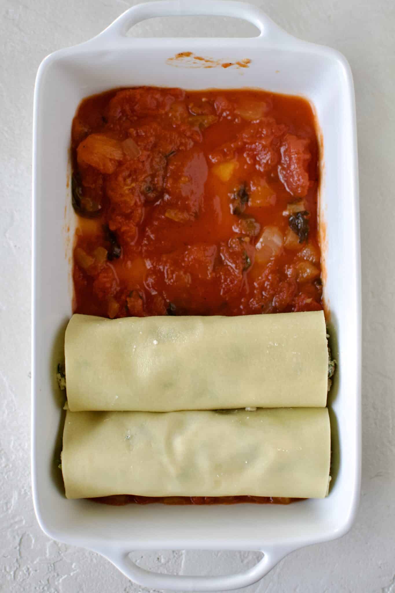 Lining up filled manicotti in a dish lined with red sauce.