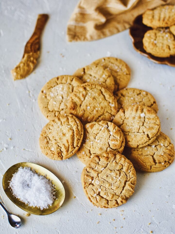 Cookies piled up on a counter sprinkled with flakey sea salt.