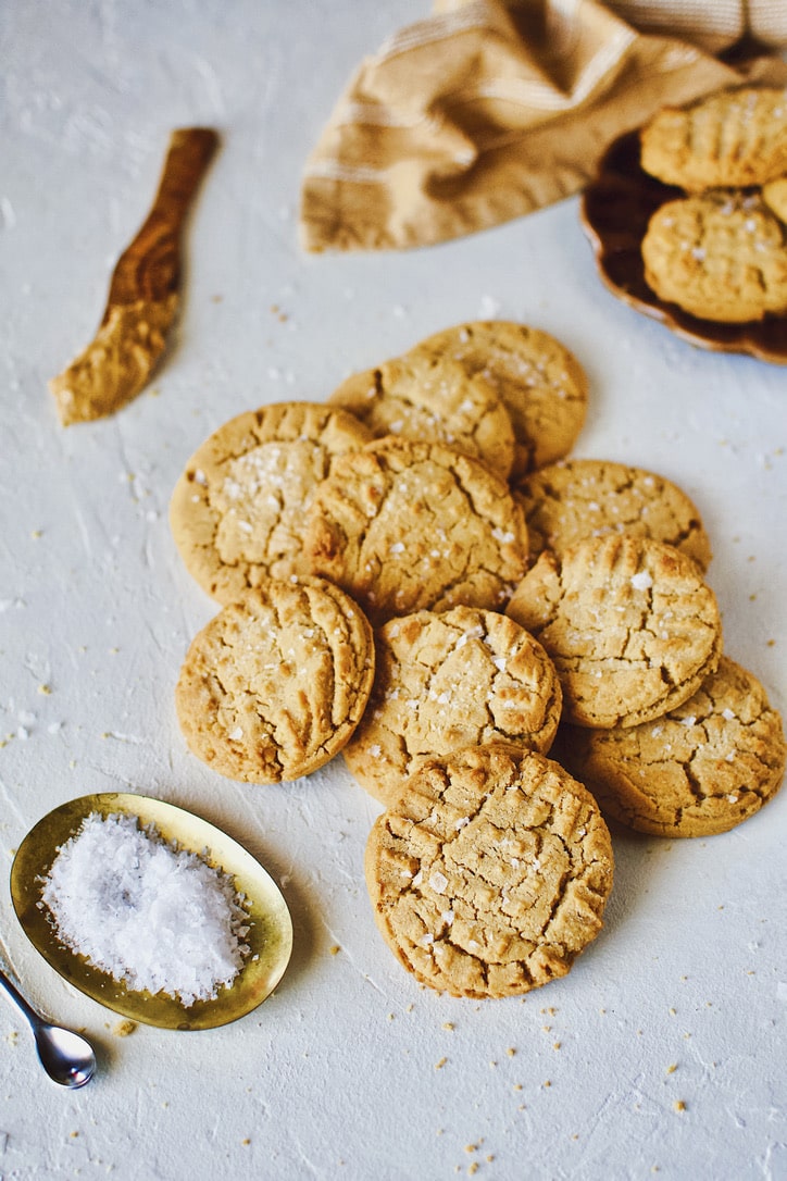 Cookies piled up on a counter sprinkled with flakey sea salt.