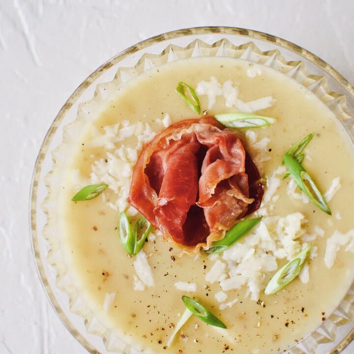 Creamy Potato Soup after blending, in a crystal bowl, topped with green onions, white cheddar, and a prosciutto rose.