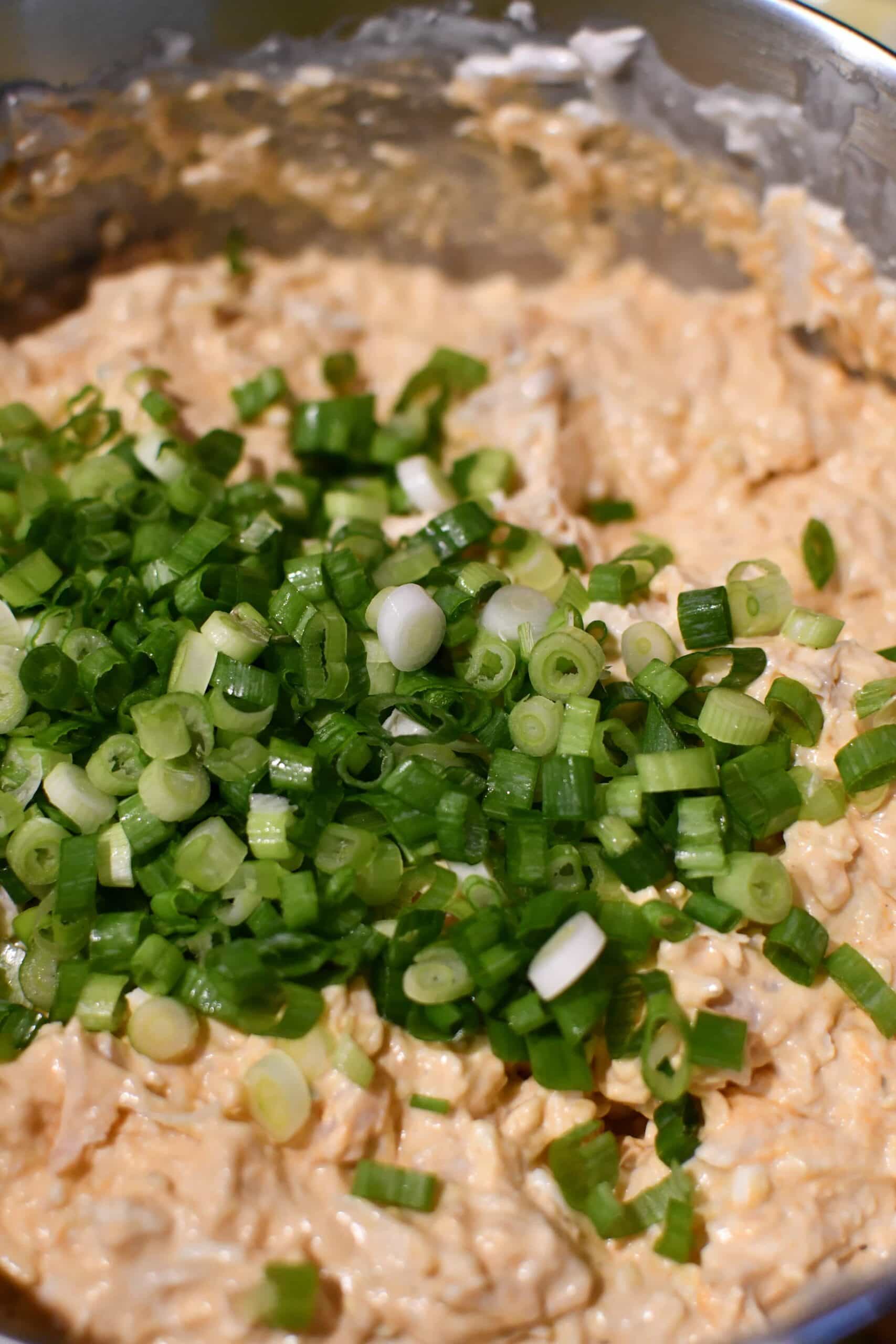 adding green onions to the bowl of the buffalo chicken cheese dip.