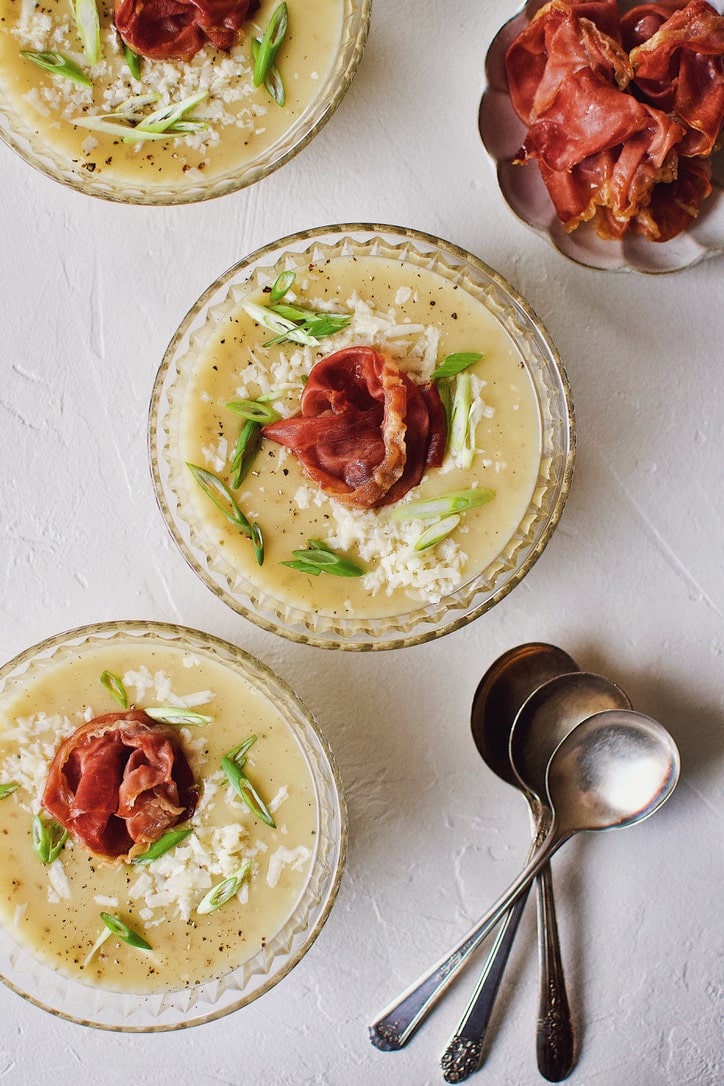 Creamy Potato Soup after blending, in a crystal bowl, topped with green onions, white cheddar, and a prosciutto rose.