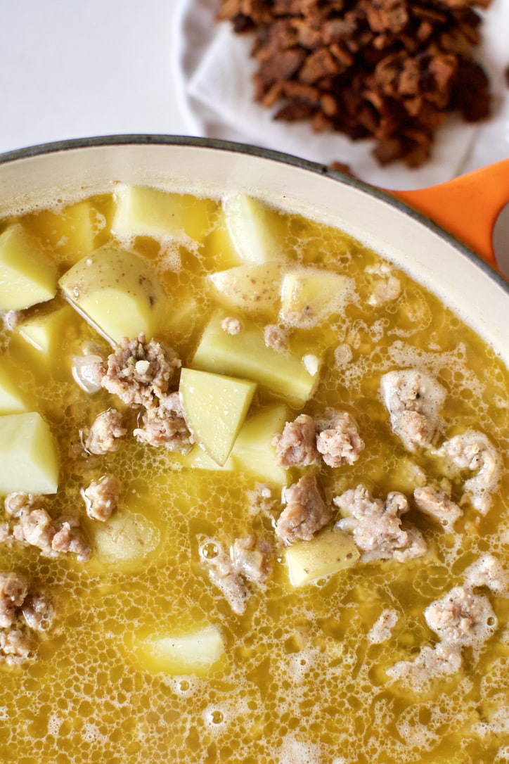 Browned sausage, chicken stock, and potatoes added to the soup pot.