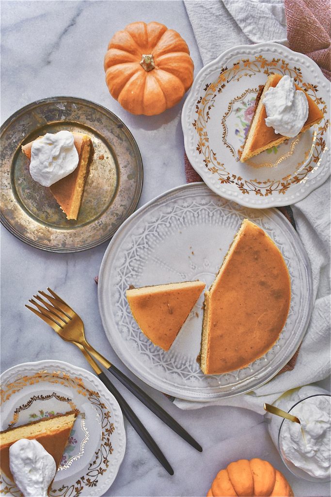 Whole sliced perfect pumpkin cheesecake on several plates on a table with pumpkins