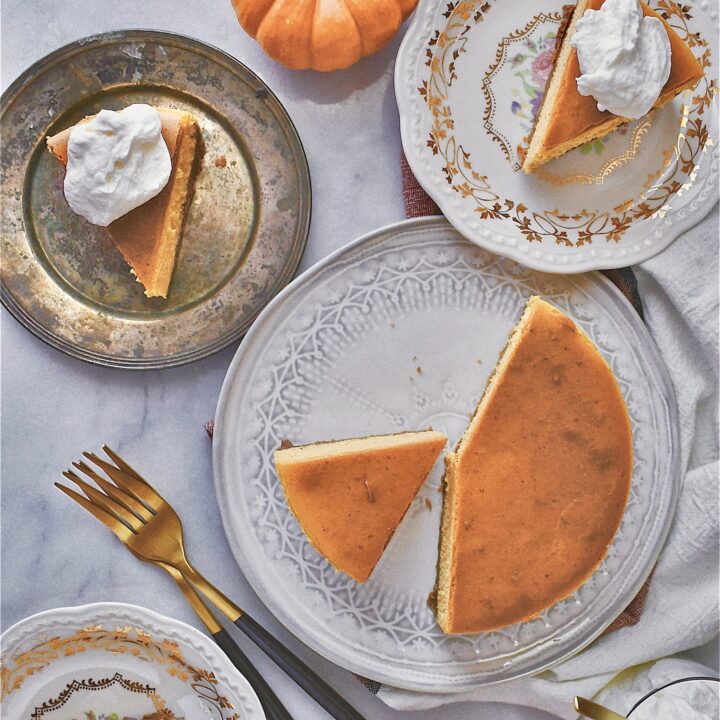 Whole sliced perfect pumpkin cheesecake on several plates on a table with pumpkins