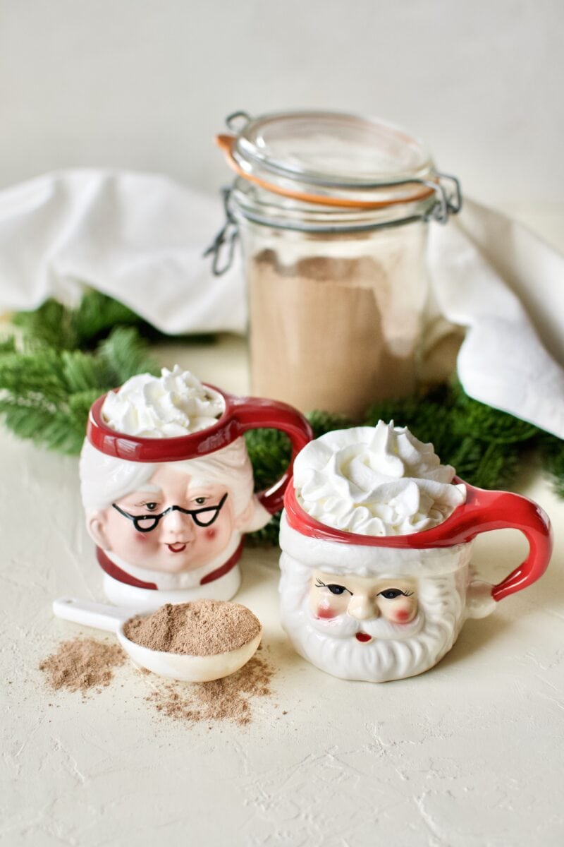 A glass of sugar-free hot cocoa in Santa and Mrs. Claus mugs topped with whipped cream.