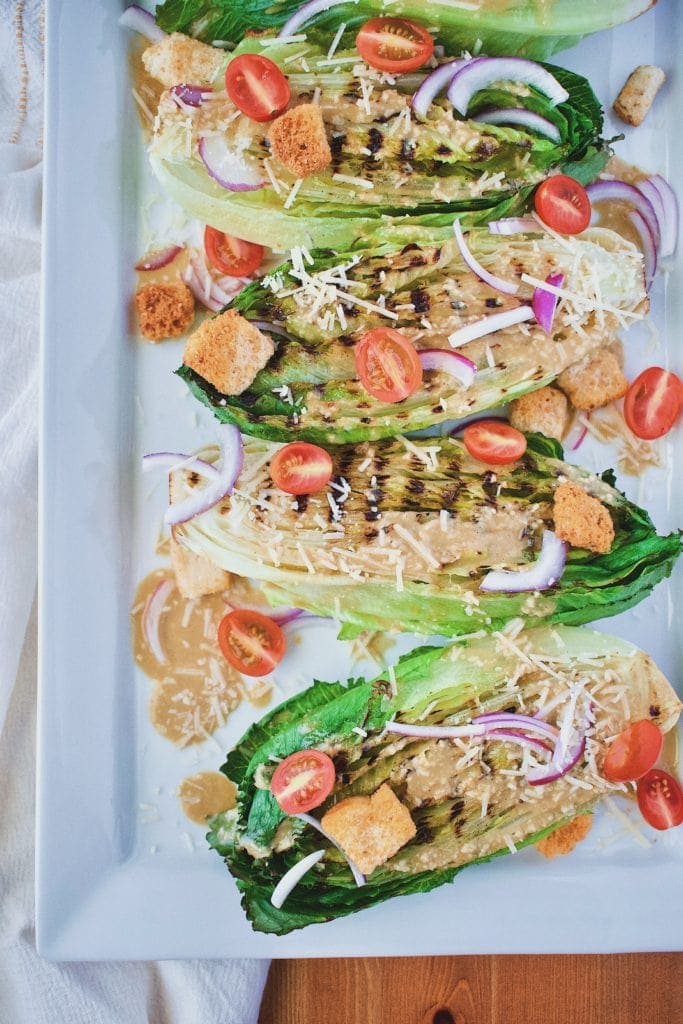 Grilled Caesar Salad on white platter with tomatoes, red onion, and parmesan cheese