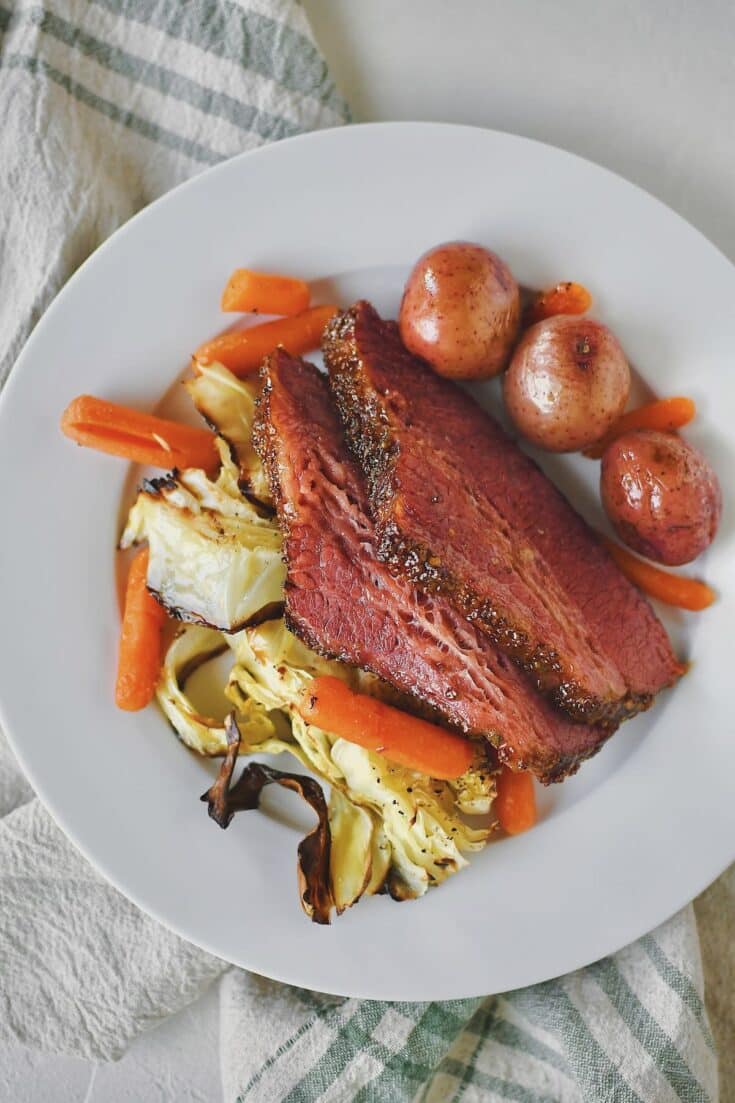 Corned Beef and Cabbage served on a plate with potatoes and carrots on the side.