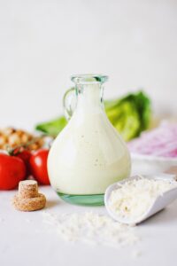 Creamy Caesar Dressing in a bottle surrounded by ingredients needed to make a Caesar Salad.