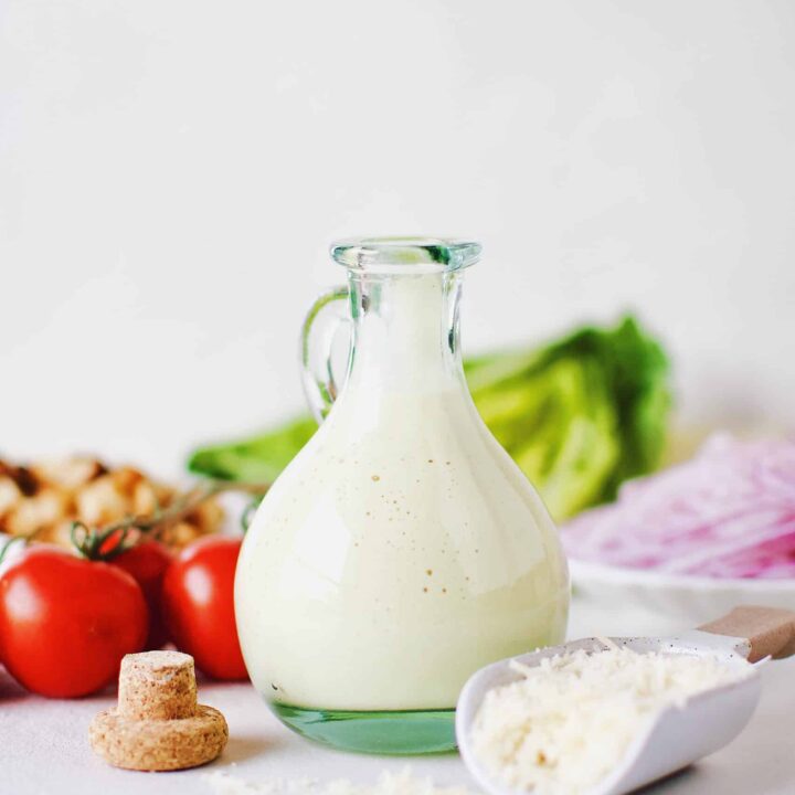 Creamy Caesar Dressing in a bottle surrounded by ingredients needed to make a Caesar Salad.