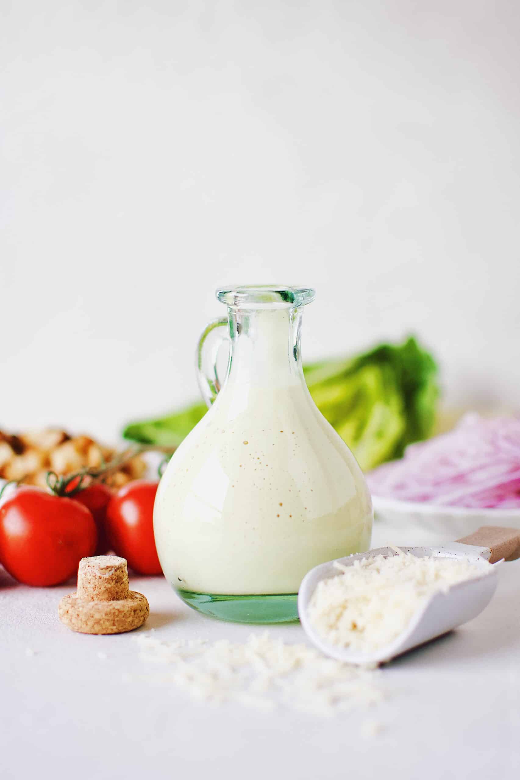 Creamy Caesar Dressing in a bottle surrounded by ingredients needed to make a Caesar Salad.