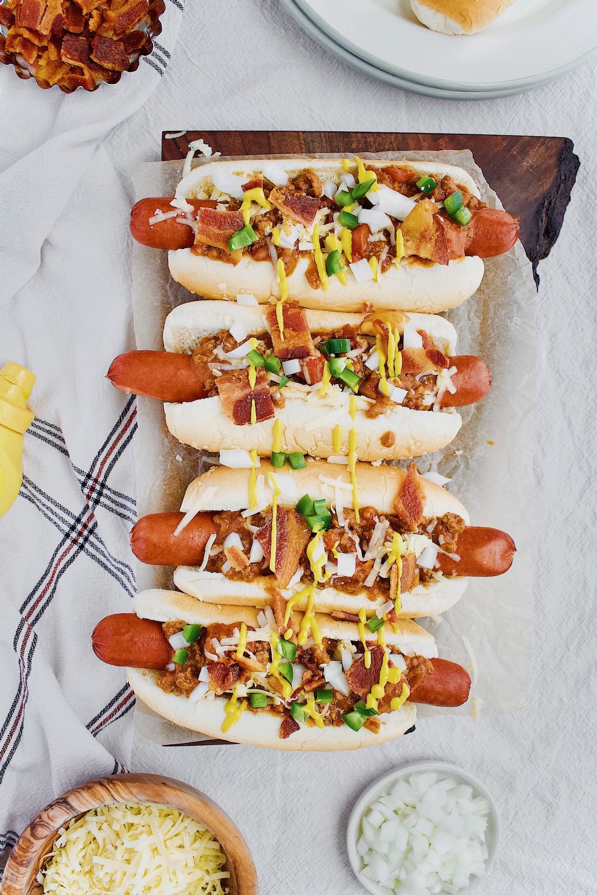 Chili Dogs lined up and topped with cheddar, onions, jalapeno, yellow mustard and Hot Dog Sauce.