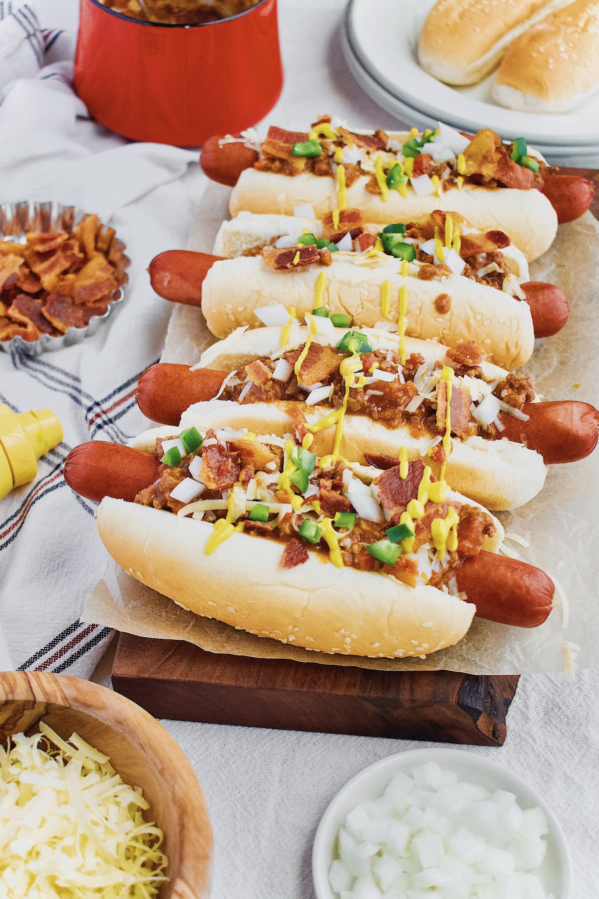 Chili Dogs lined up and topped with cheddar, onions, jalapeno, yellow mustard and Hot Dog Sauce.