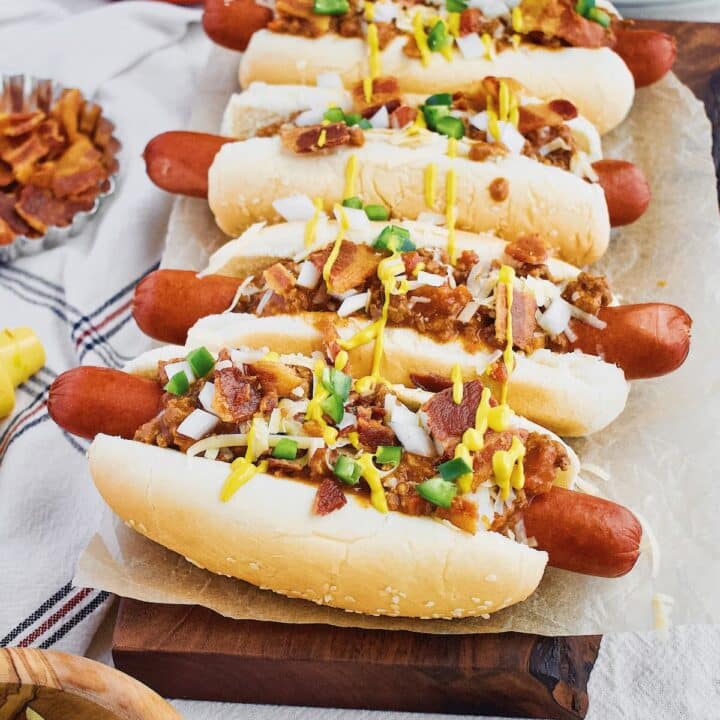 Chili Dogs lined up and topped with cheddar, onions, jalapeno, yellow mustard and Hot Dog Sauce.