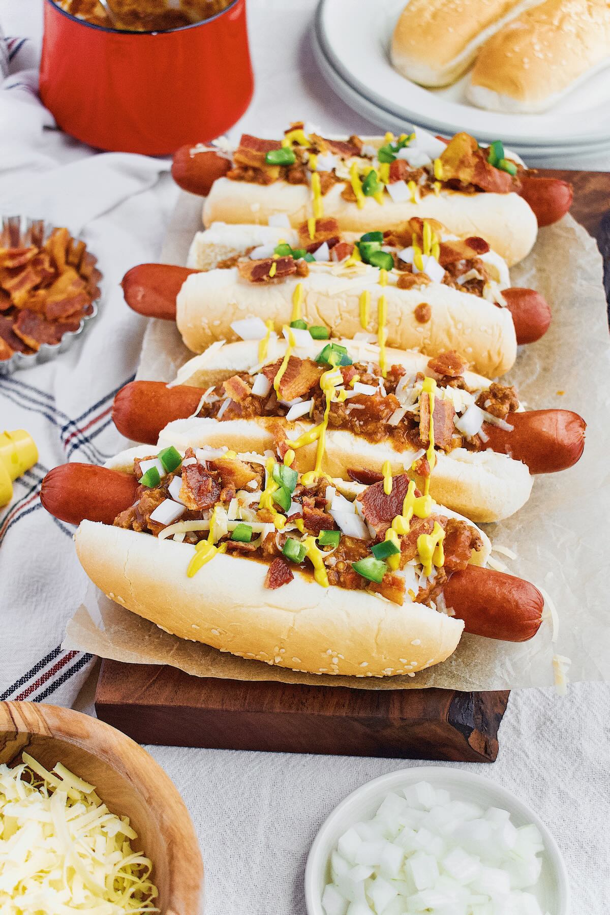 Chili Dogs lined up and topped with cheddar, onions, jalapeno, yellow mustard and Hot Dog Sauce.