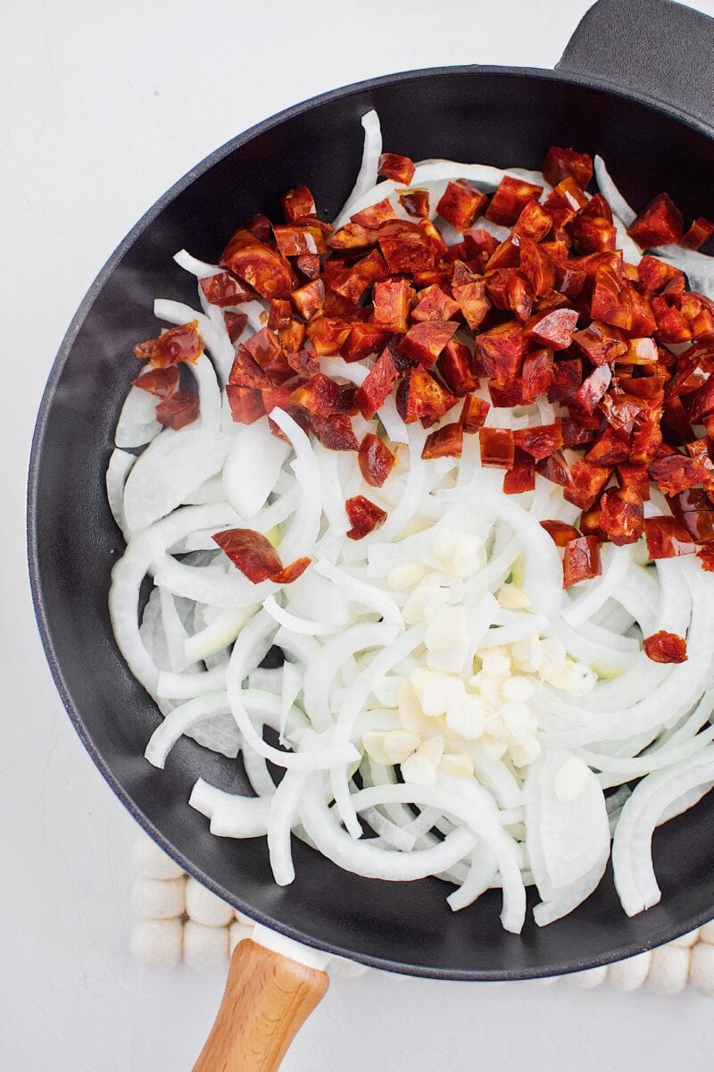 Sliced onion, garlic, and diced chorizo in a cast iron pan