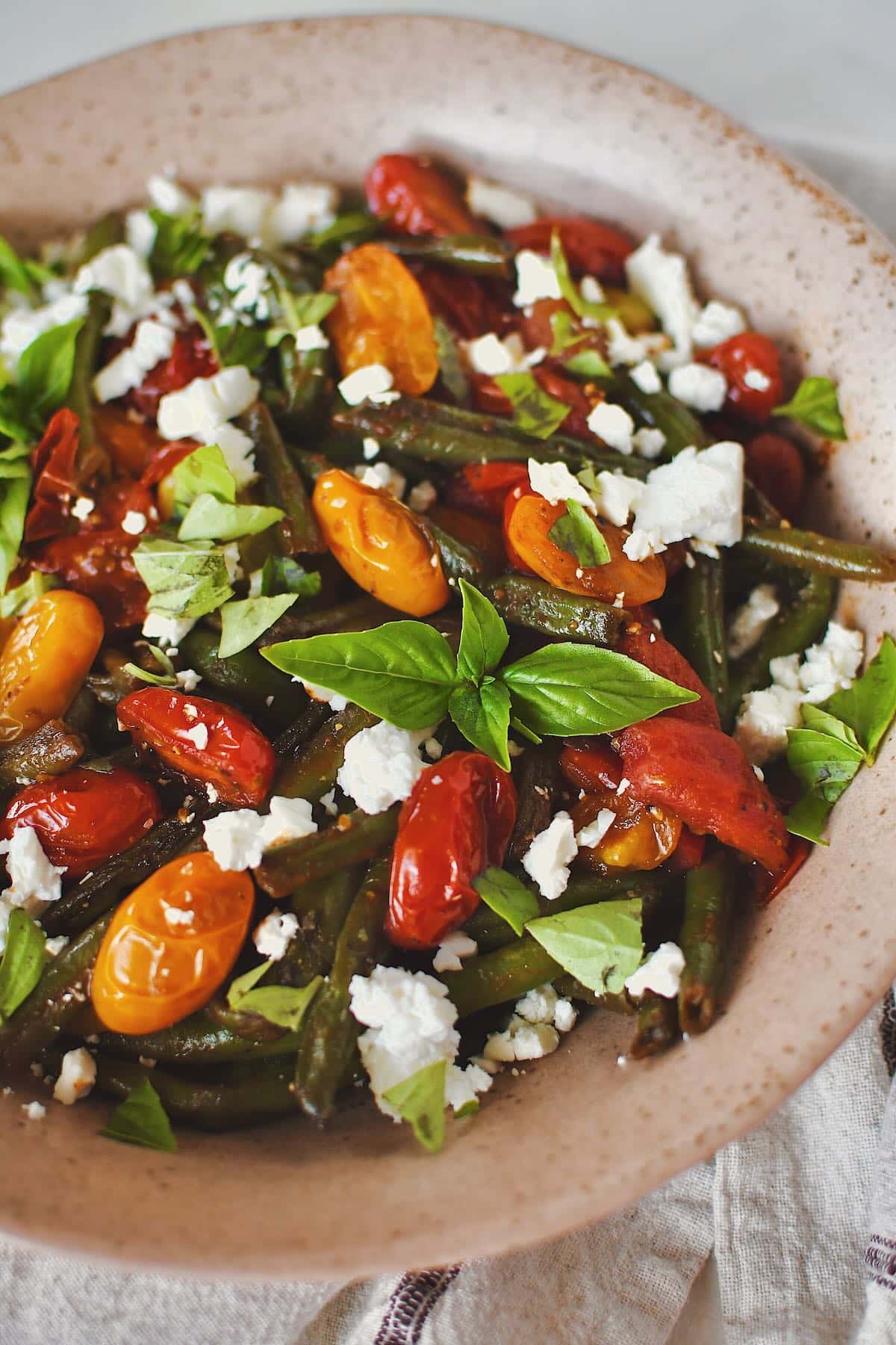 Green Bean Salad, in a serving bowl, topped with feta and basil, ready to eat.