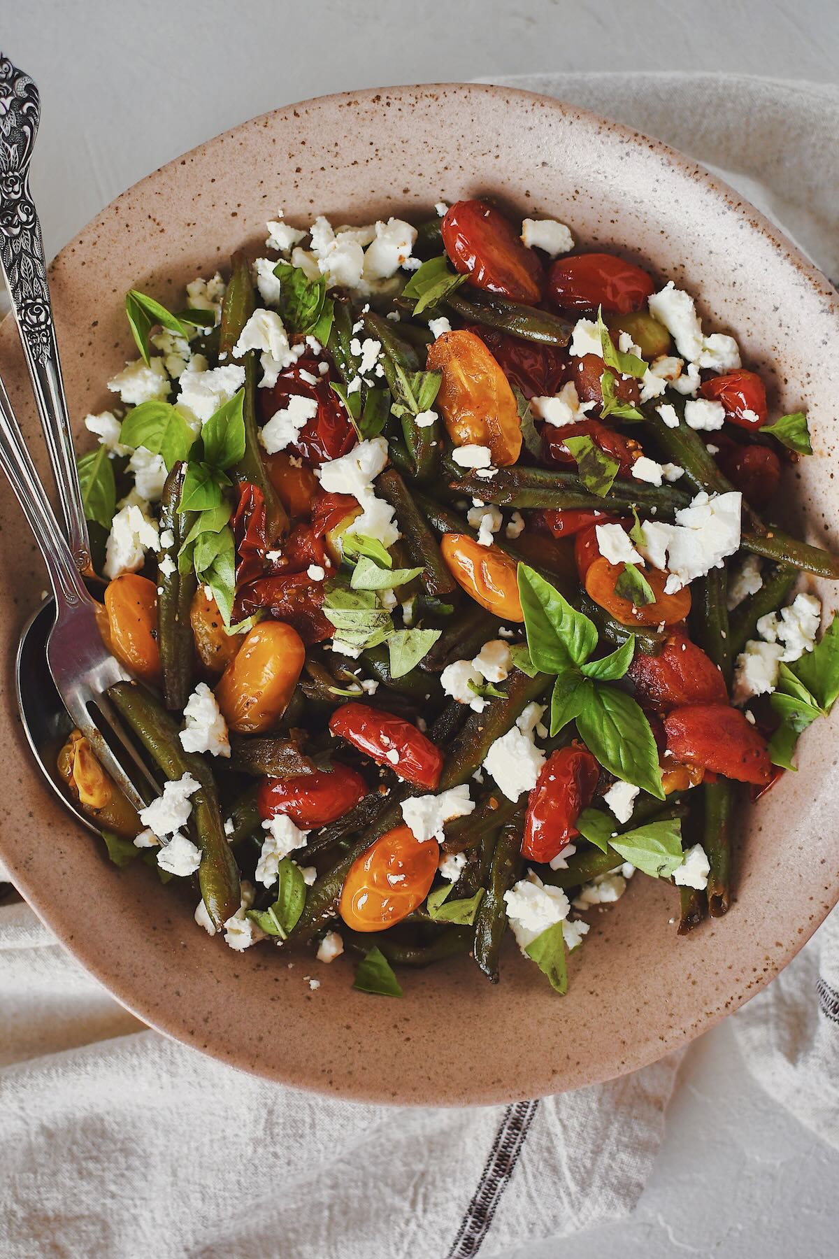 Green Bean Salad, in a serving bowl, topped with feta and basil, ready to eat.