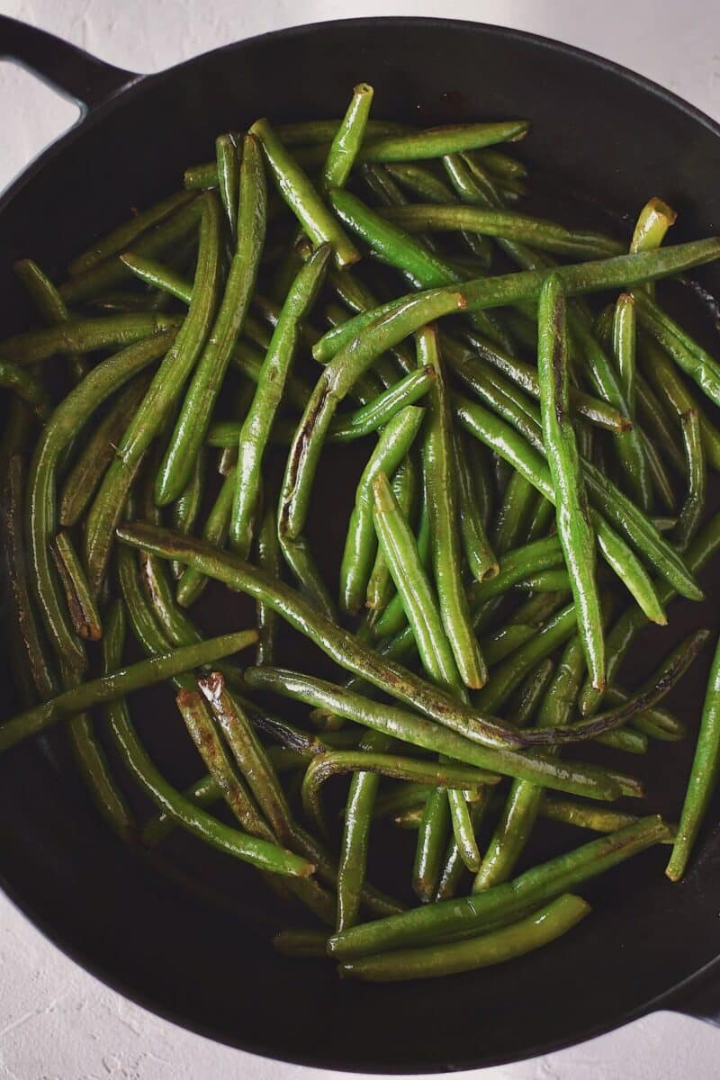 Cooking the green beans in olive oil, in a large skillet till the begin to brown.