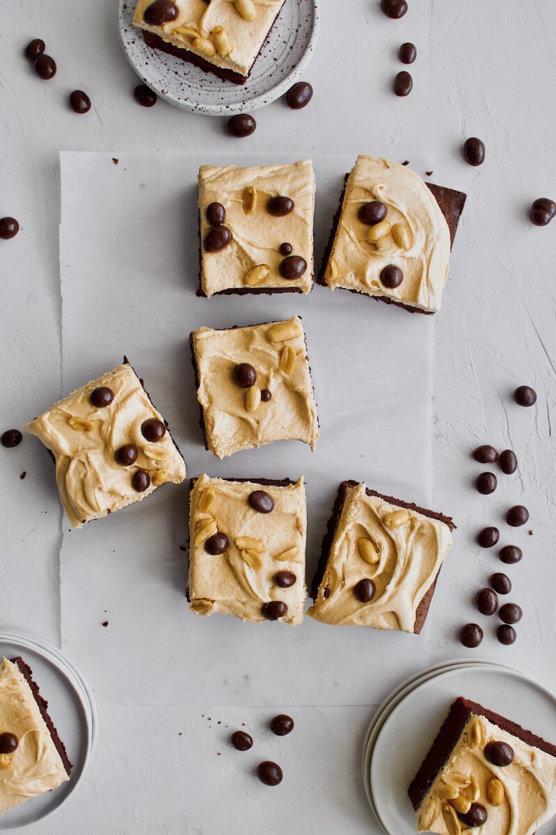 Chocolate Covered Peanut Cake sliced and ready to serve on white plates with extra peanuts scattered around