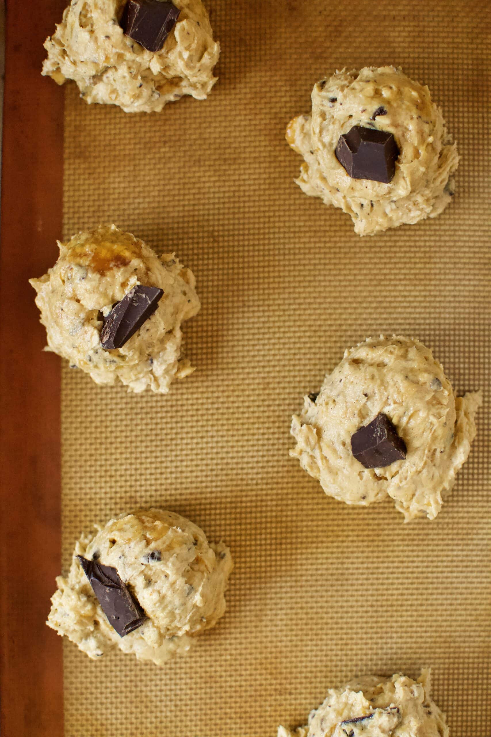 cookies portioned out on to a tray with a chocolate chunk placed on top, ready to bake