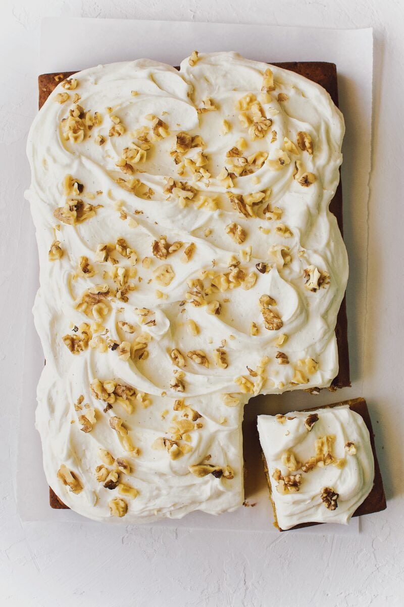 Finished pumpkin cake topped with cream cheese frosting and walnuts with a single slice cut from it