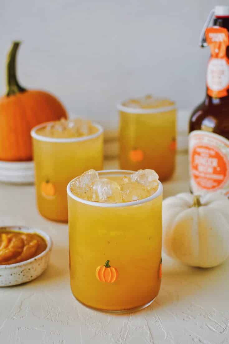 3 glasses of pumpkin juice in a row with baby pumpkin all around on a white background