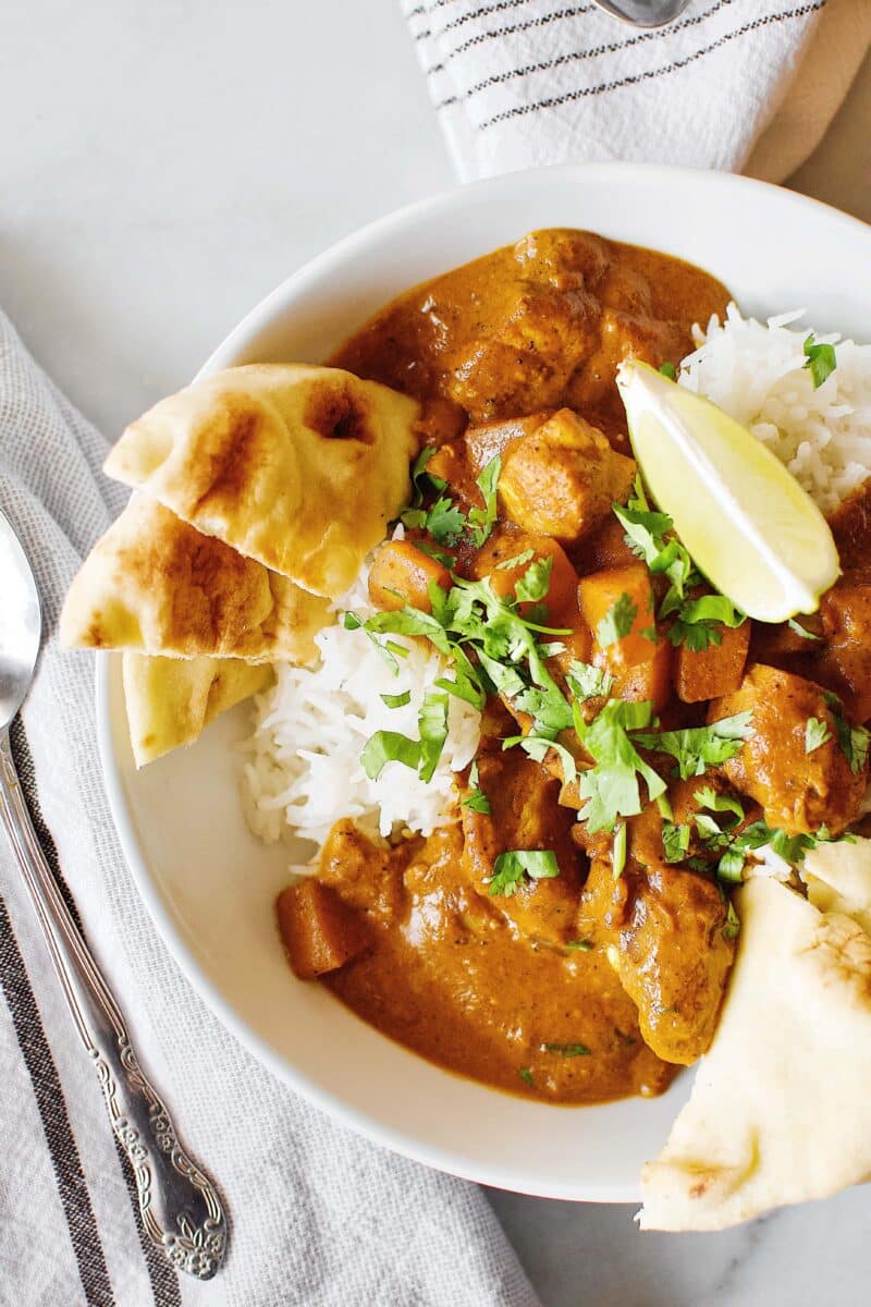 Pumpkin Butter Chicken recipe served with basmati rice, cilantro, naan, and lime wedges.