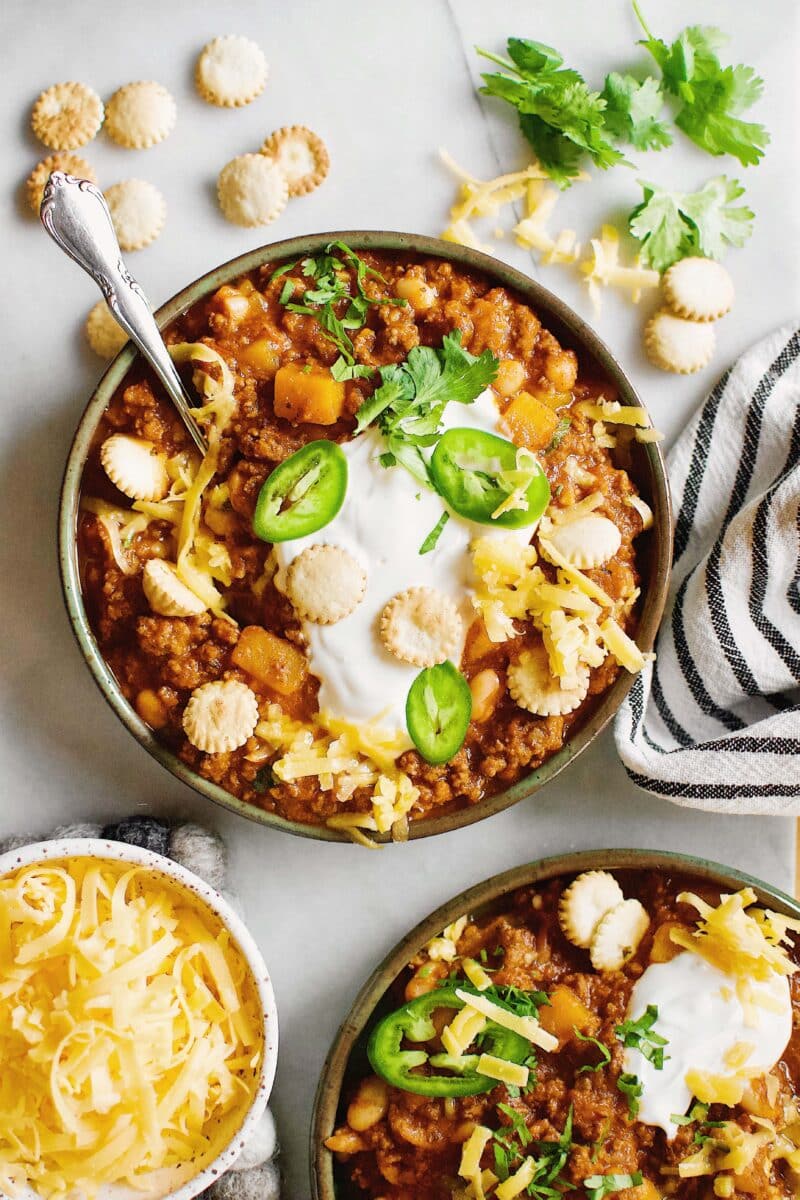 Two bowls of Pumpkin Chili garnished with oyster crackers, cilantro, jalapeno and cheese.