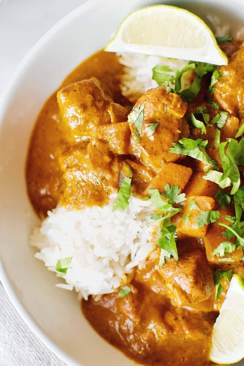 Pumpkin Butter Chicken recipe served of basmati rice with cilantro and lime wedges.