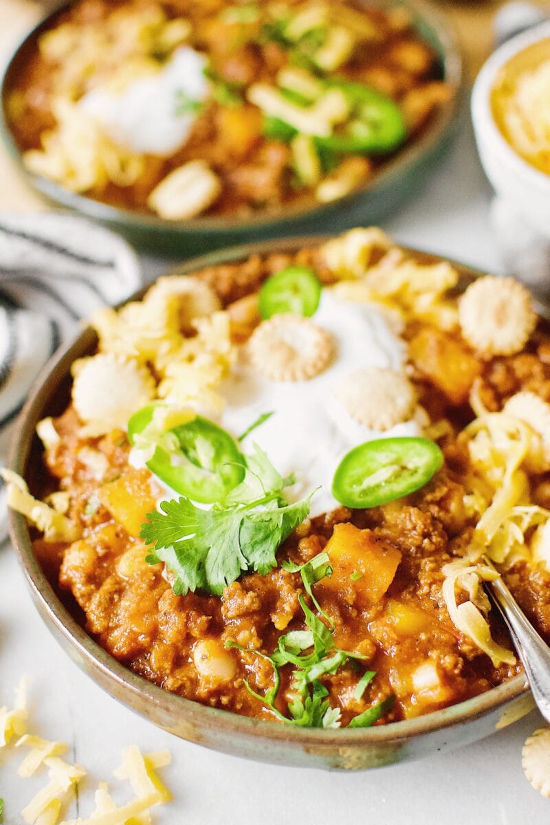 Two bowls of Pumpkin Chili garnished with oyster crackers, cilantro, jalapeno and cheese.