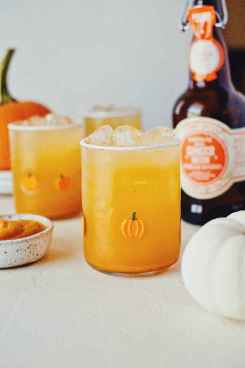 3 glasses of pumpkin juice in a row with baby pumpkin all around on a white background