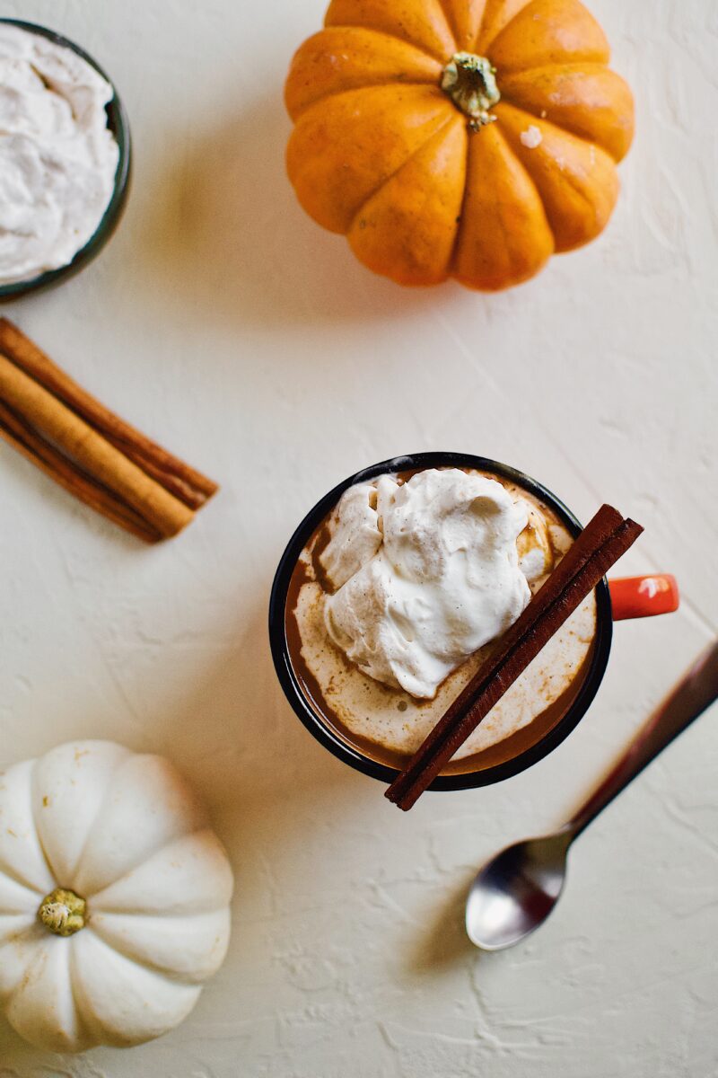 Pumpkin Spice Hot Chocolate in an orange camp mug topped with chai whipped cream and a cinnamon stick