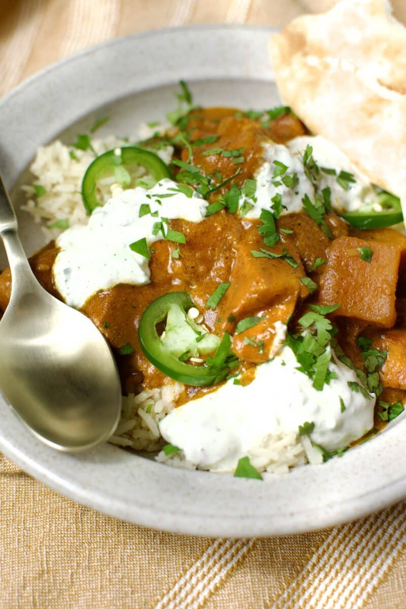 Pumpkin Butter Chicken served with basmati rice, cilantro, naan, and lime wedges.