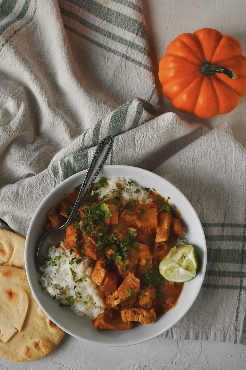 Looking into a bowl of Pumpkin Butter Chicken served over rice with naan bread on the side.