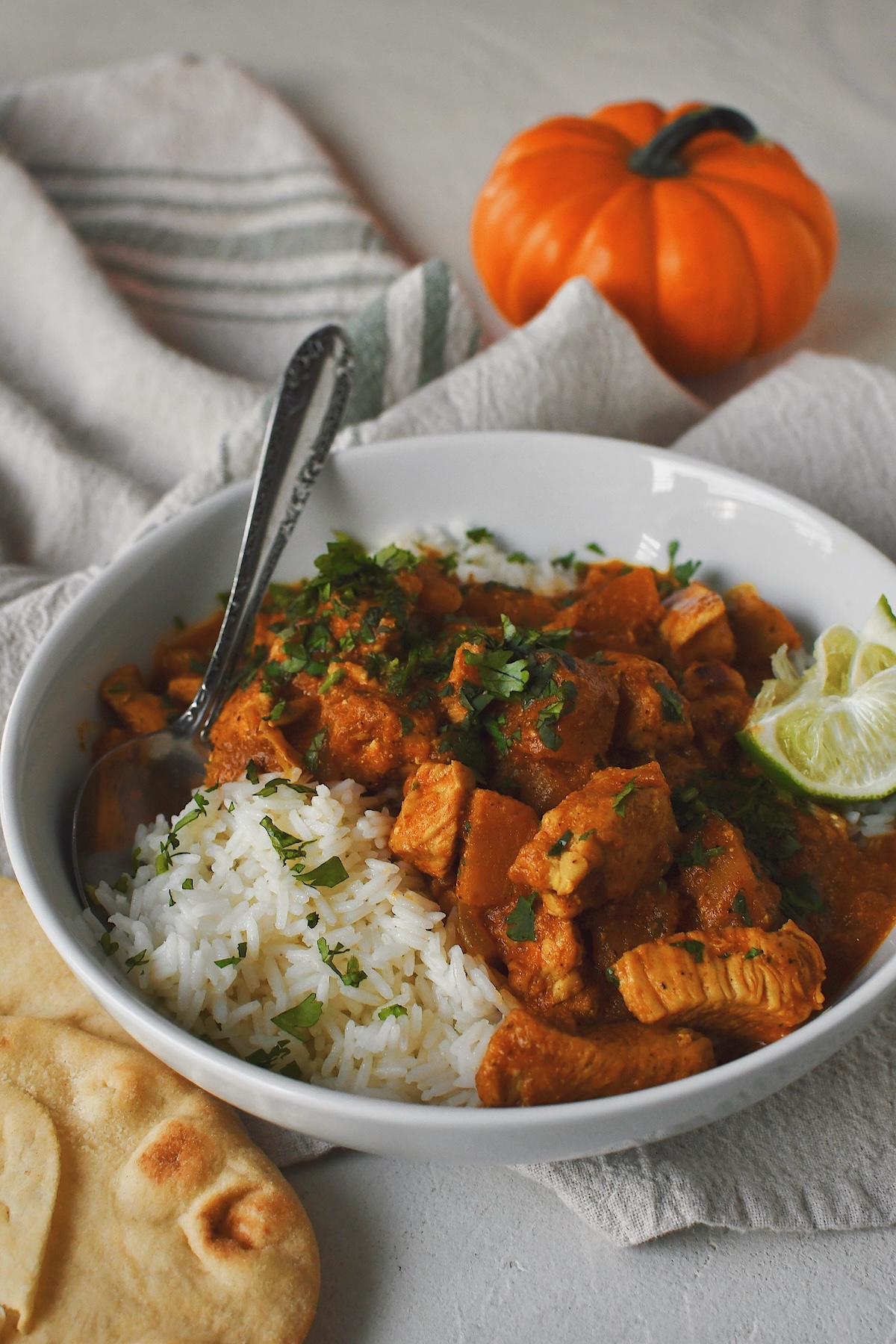 Pumpkin Butter Chicken, with a pumpkin in the background, served over rice and naan bread for dipping.