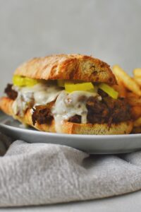 Looking into a pot roast sandwich with a side of fries on a plate.