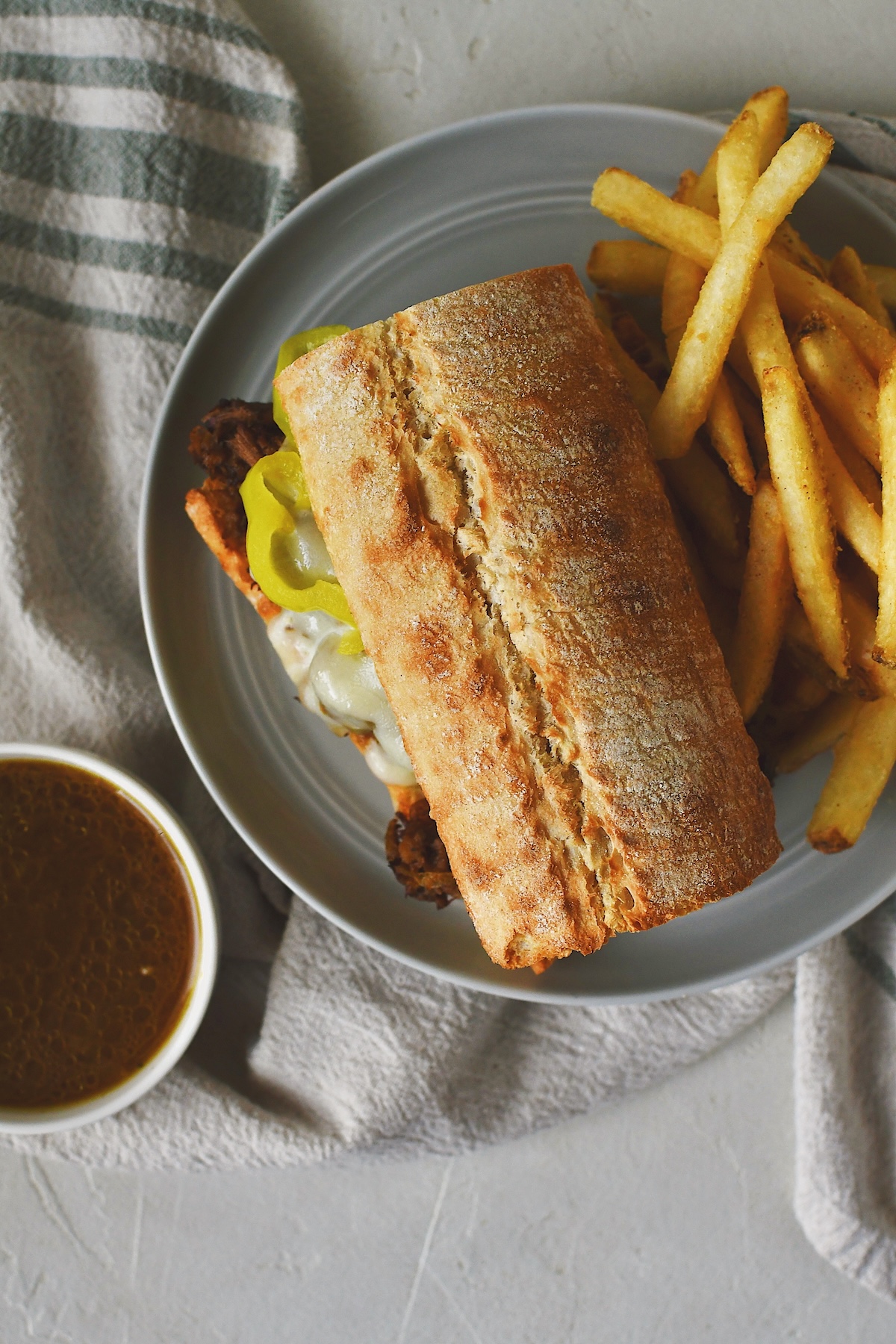 Looking down at a pot roast sandwich with a side of fries and jus for dipping.