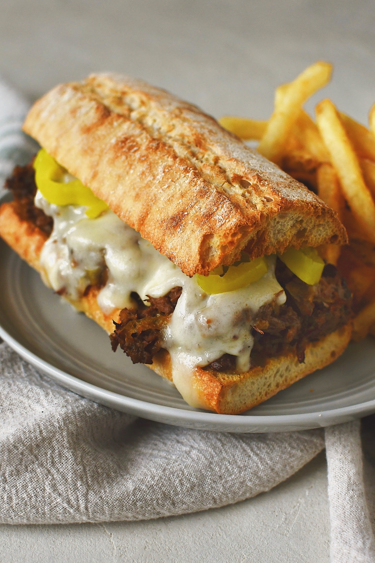 Looking at a side profile of a pot roast sandwich with a side of fries and jus for dipping.