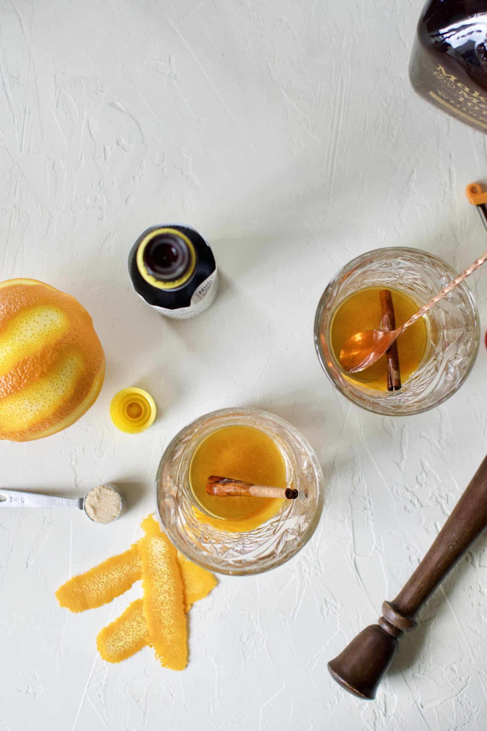 adding the orange peel and cinnamon stick to the muddled brown sugar, water, and bitters in the bottom of a glass.