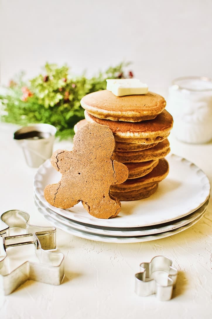 A stack of Gingerbread Pancakes with a Gingerbread Person shaped pancakes standing in front of the stack.