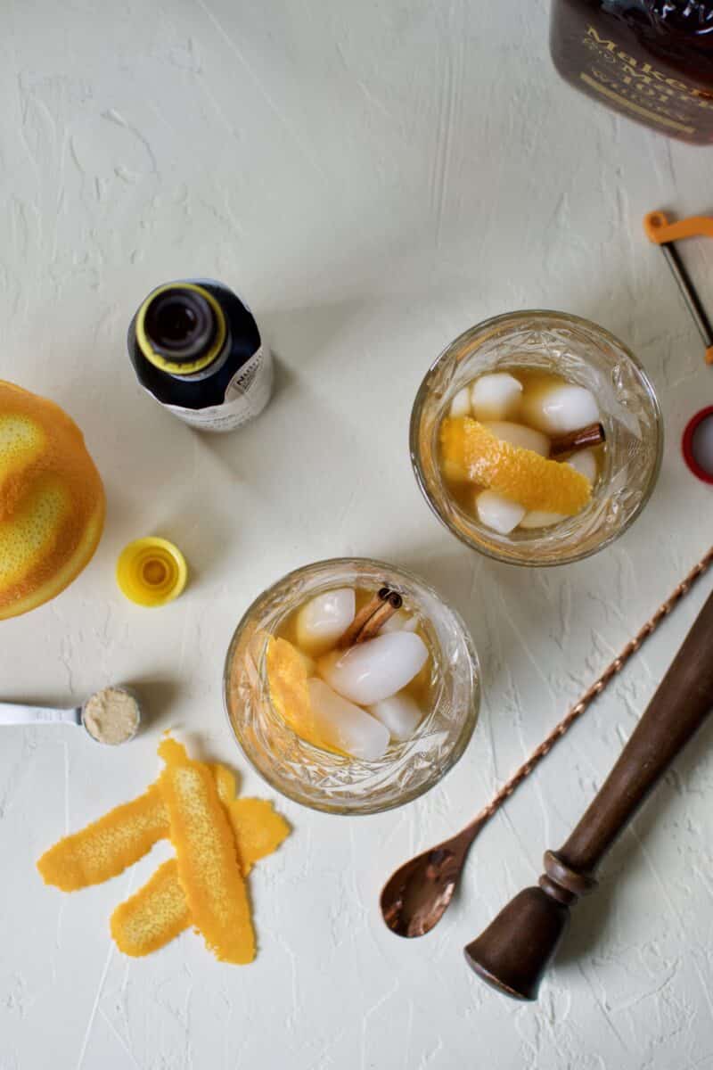 bourbon and ice added to the orange peel and cinnamon stick to the muddled brown sugar, water, and bitters in the bottom of a glass.