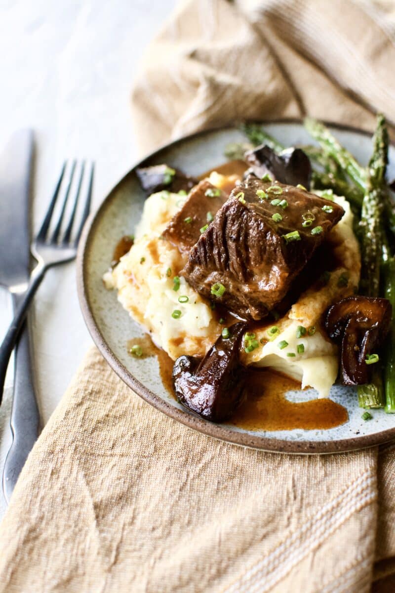 Red Wine Braised Short Ribs recipe on a bed of mashed potatoes with broiled asparagus around them.