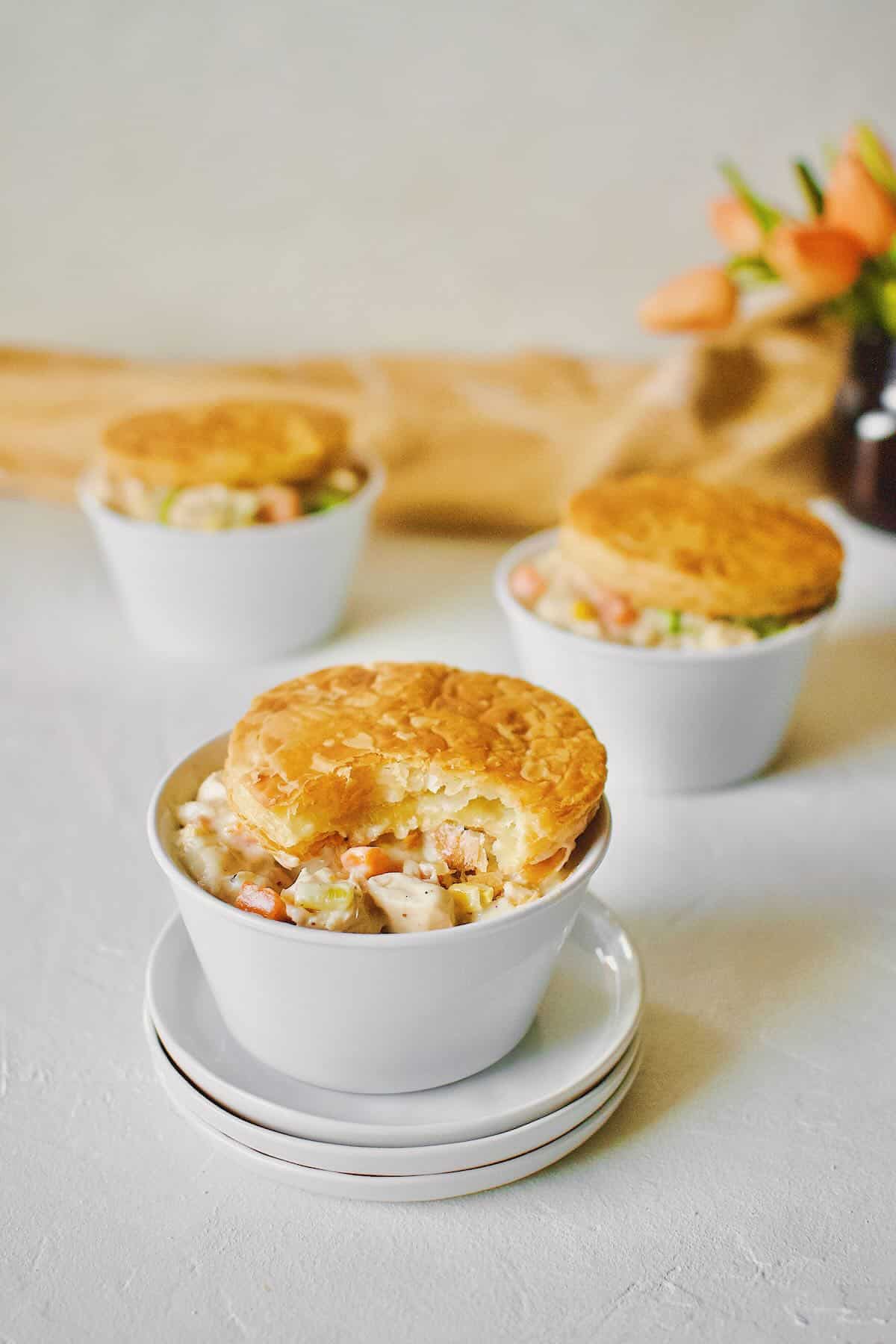 3 individual Chicken Pot Pie with Puff Pastry tops. One with a bite taken out of it.