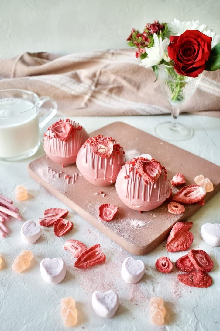 Pink Hot Chocolate Bombs ready to be enjoyed and a warm mug of milk in the back.