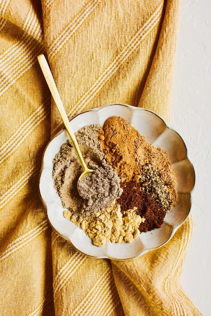 Chai Spice Mix spices portioned out on a plate, with a gold spoon in it ready to stir it up.