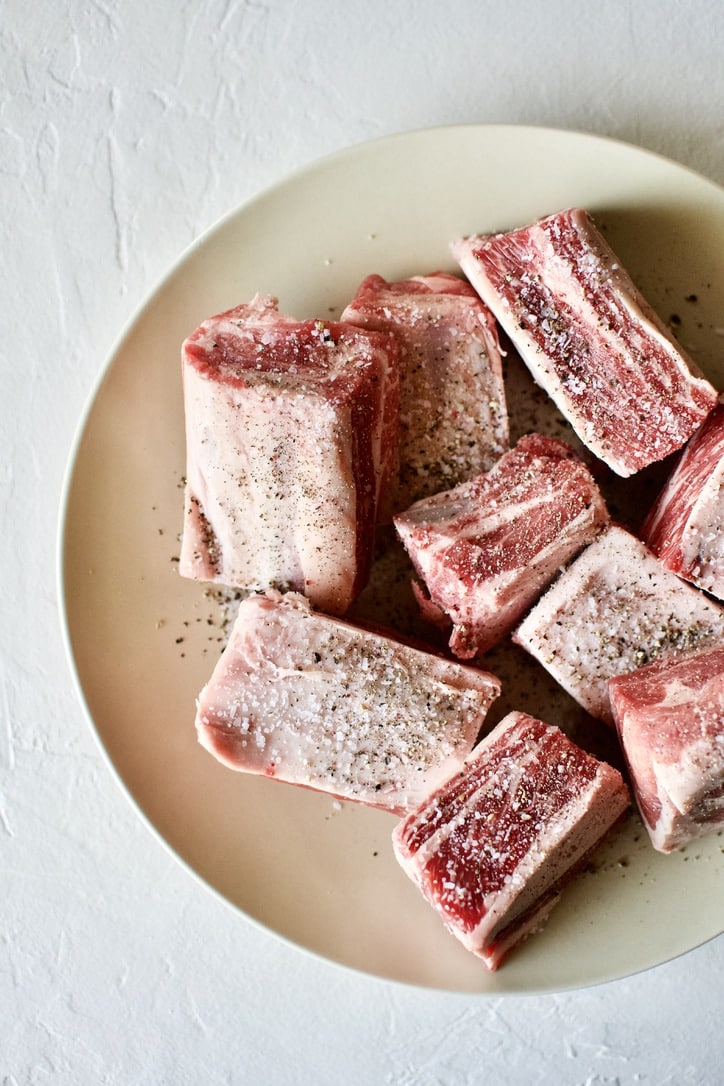 Short Ribs on a plate seasoned with salt and pepper in preparation for Red Wine Braised Short Ribs recipe.