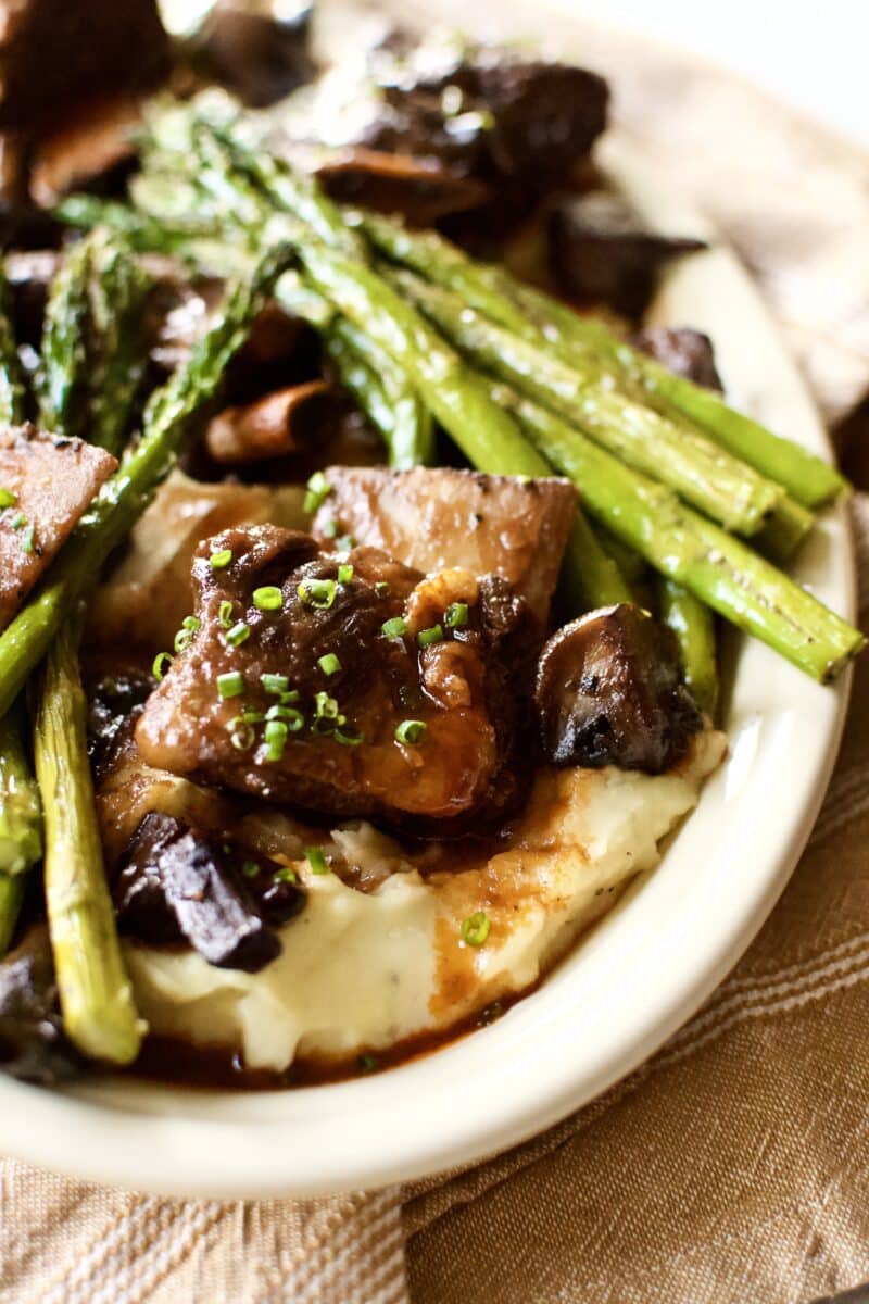 Red Wine Braised Short Ribs on a bed of mashed potatoes with broiled asparagus around them.