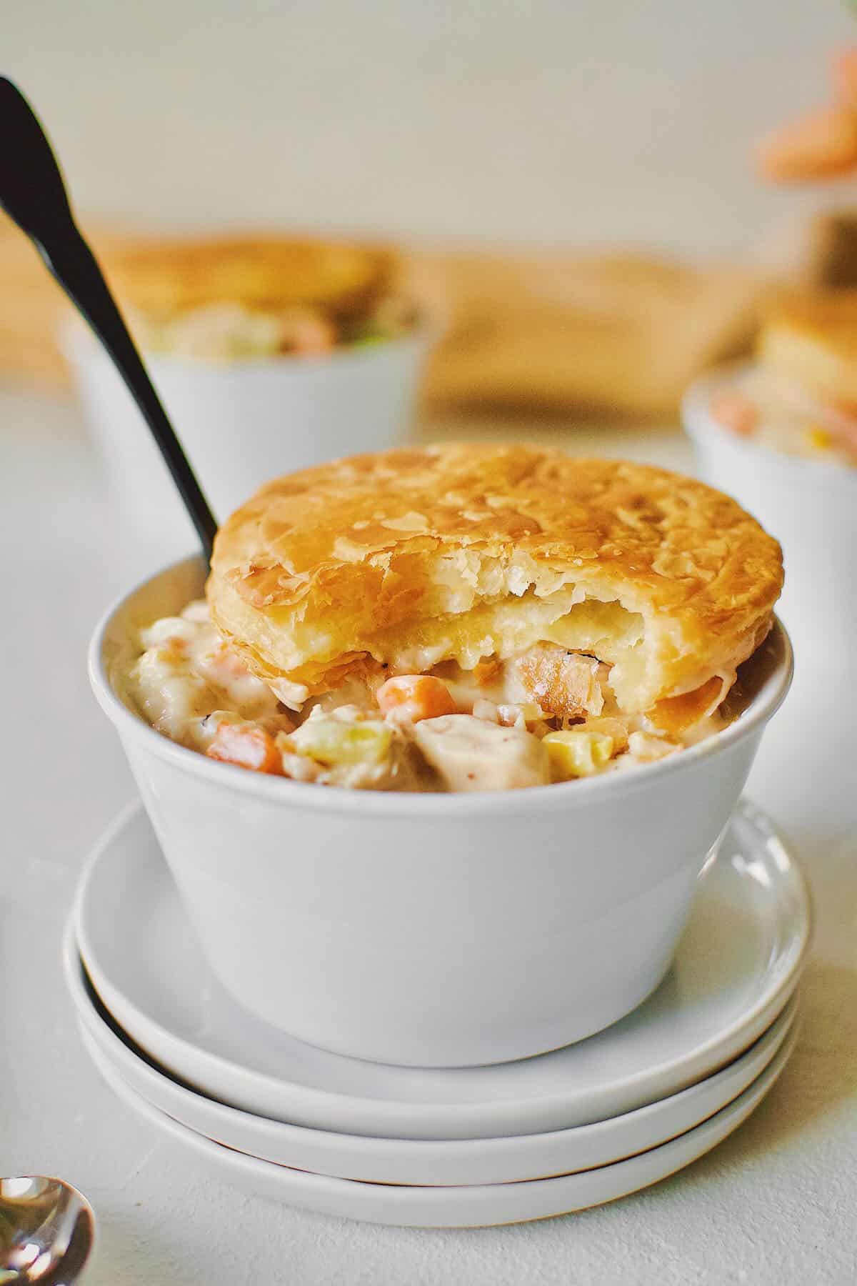 3 individual Chicken Pot Pie with Puff Pastry tops. One with a bite taken out of it.